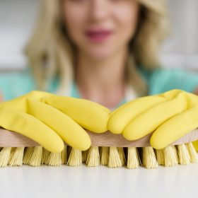 close-up-woman-s-hand-holding-brush-cleaning-white-table